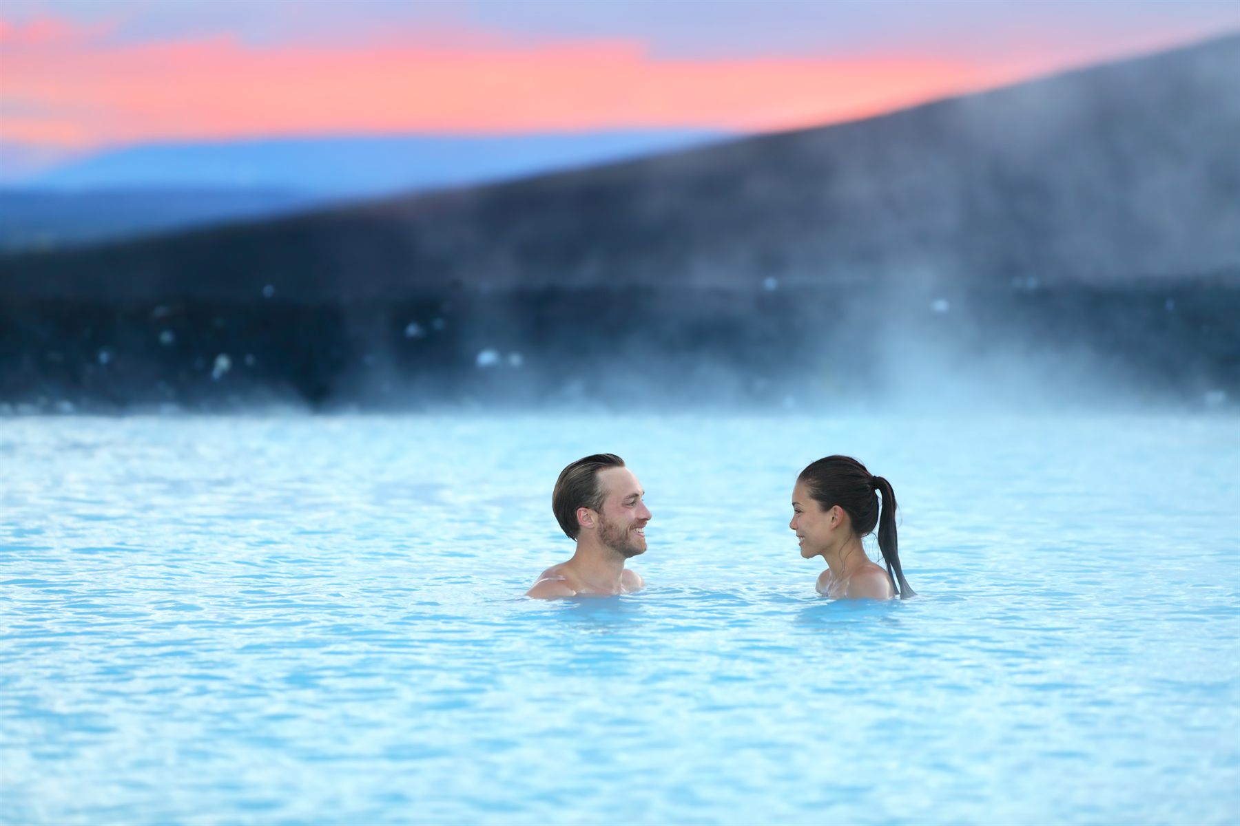 A couple bathing in the steaming milky-blue water of a geothermal lagoon in Iceland