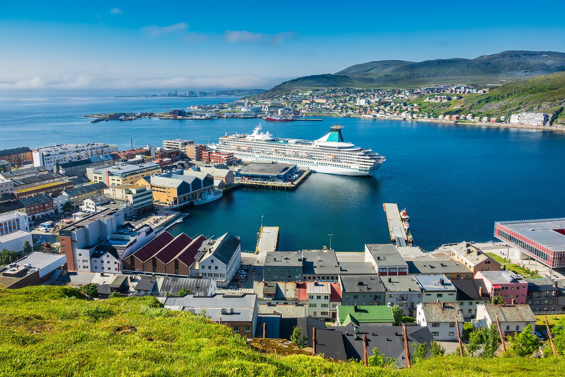 A cruise ship docked in a small Arctic Norwegian harbor town seen from the hillside
