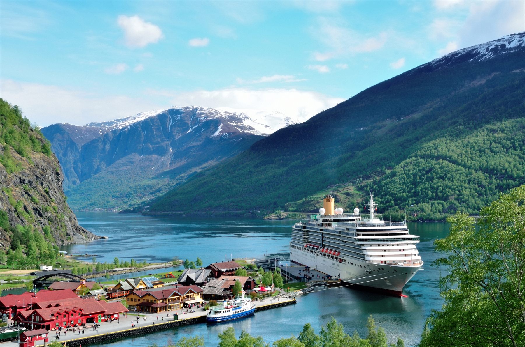 A cruise ship docked at a fjord village below steep green mountains in Norway